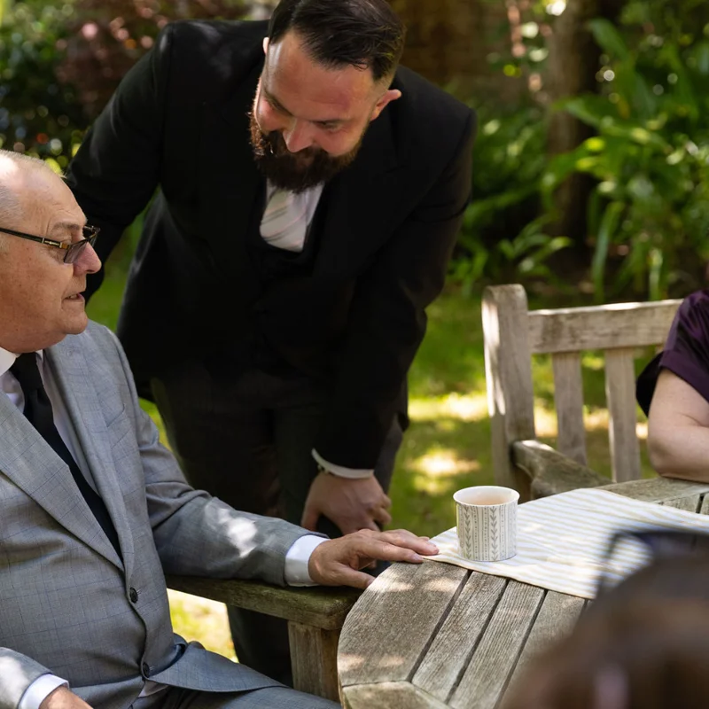 Family gathered around a table during a memorial event in a peaceful garden environment.