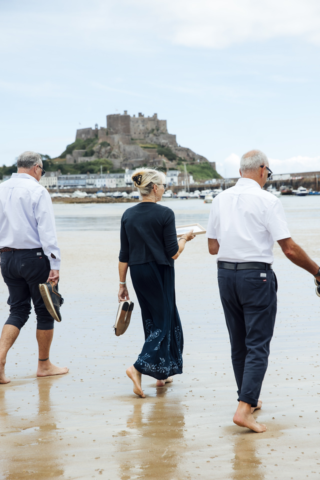 Three family members walk along the beach towards Gorey Castle, carrying their shoes.