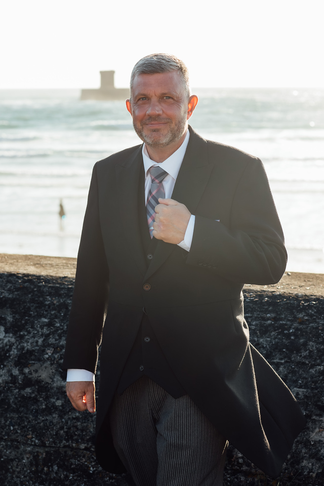 Funeral care professional in formal dress standing outdoors at St Ouen's Bay.
