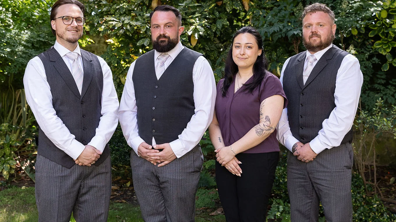 The funeral team standing together in a garden with green bushes behind them.