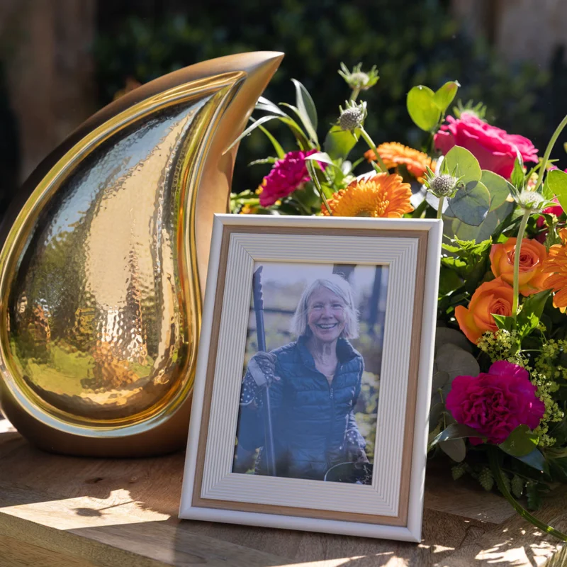 Memorial display featuring a decorative urn, framed photograph and colourful floral arrangement on a wooden table.