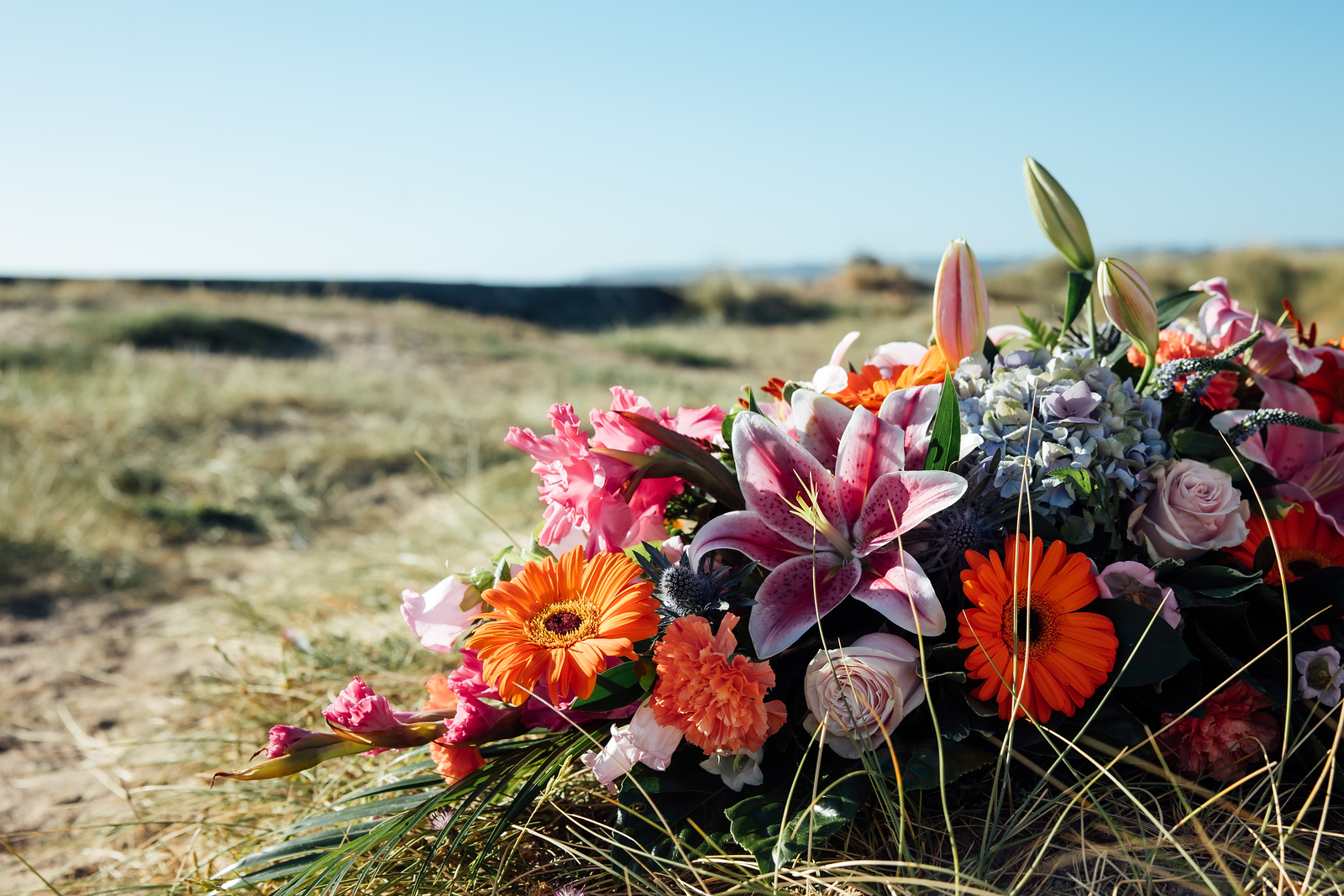 Funeral flower arrangement featuring lilies, roses and gerbera flowers in a peaceful outdoor location.