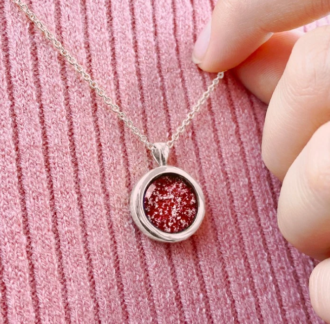 Round memorial pendant necklace featuring a red remembrance stone, worn close to the heart as a tribute to a loved one.