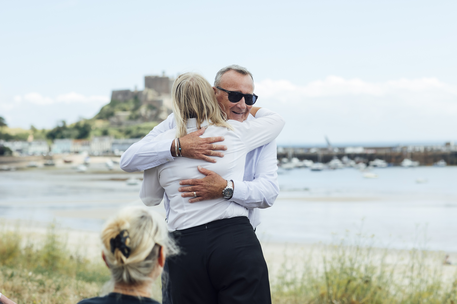 A man embraces a woman by the harbour, with Gorey Castle in the background.