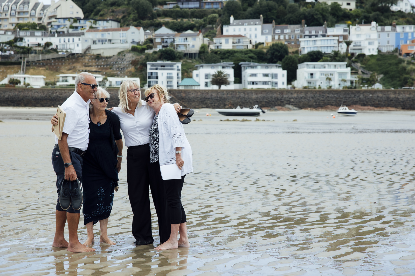 Four family members stand together on the beach, smiling with their arms around each other.