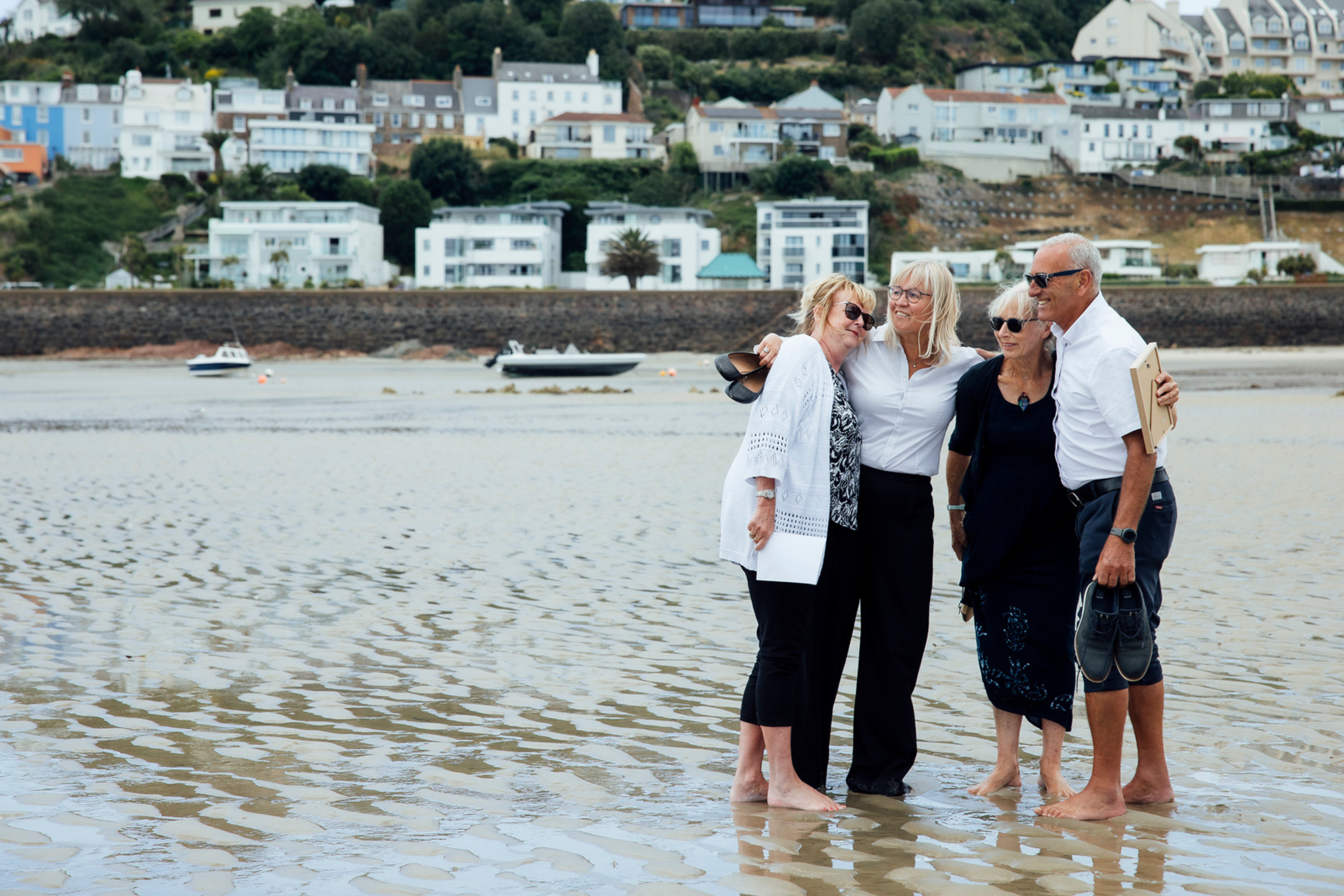 Four family members stand together on the beach, smiling with their arms around each other.